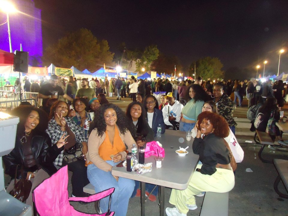 From Queens, With Love members gathered around a table at an outdoor evening event.